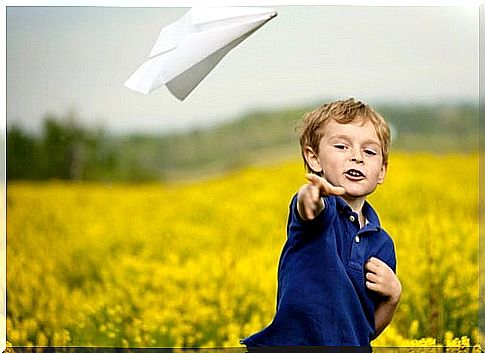 little boy throwing a paper airplane on a flower field