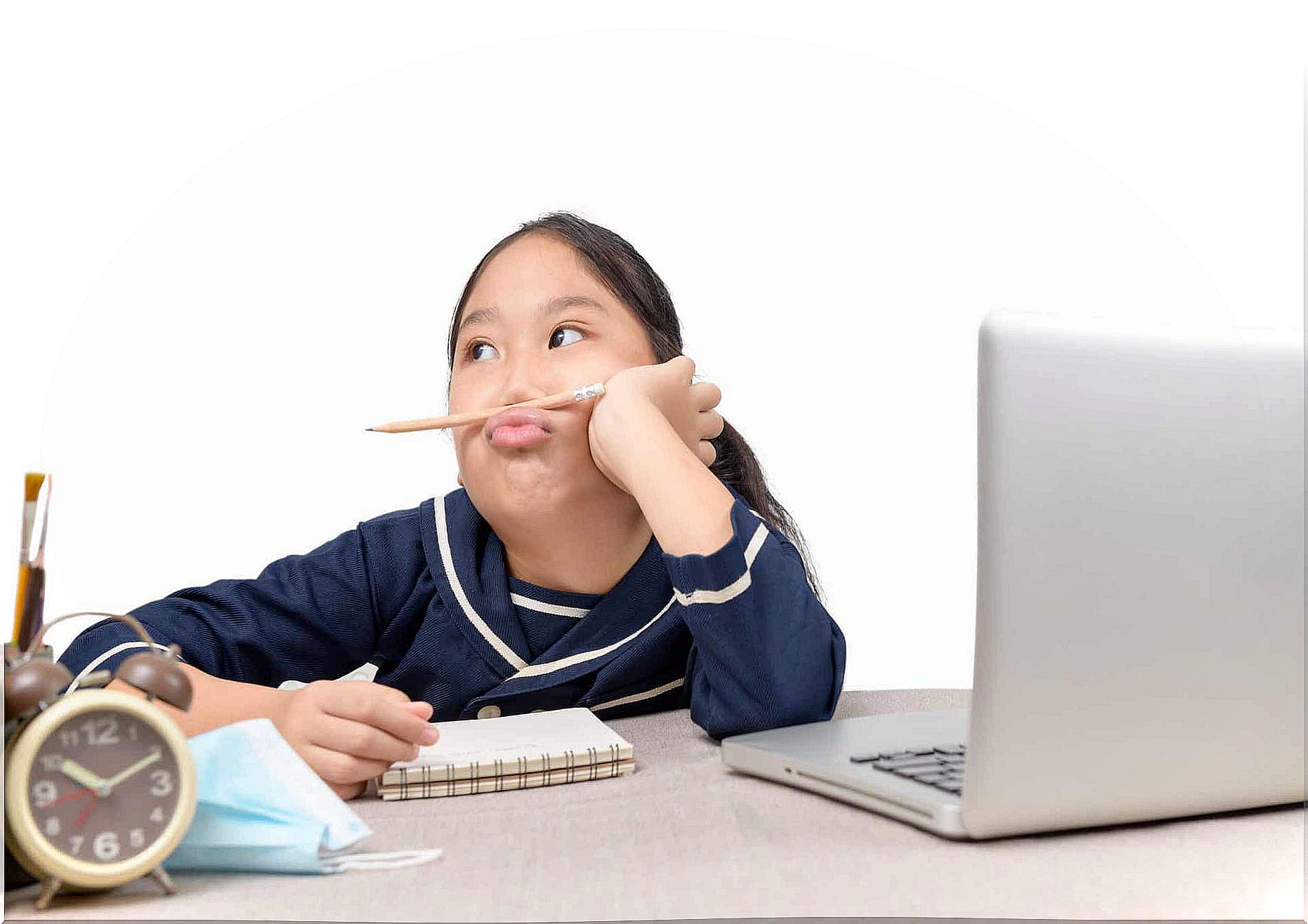 A girl sitting at a laptop looks away and plays with a pencil