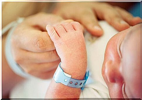 newborn baby with hospital bracelet holding finger